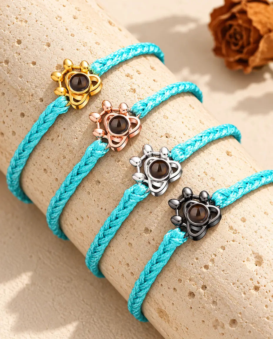 Four blue braided cord bracelets with gold tone, rose gold tone, silver and black paw charms on a travertine block