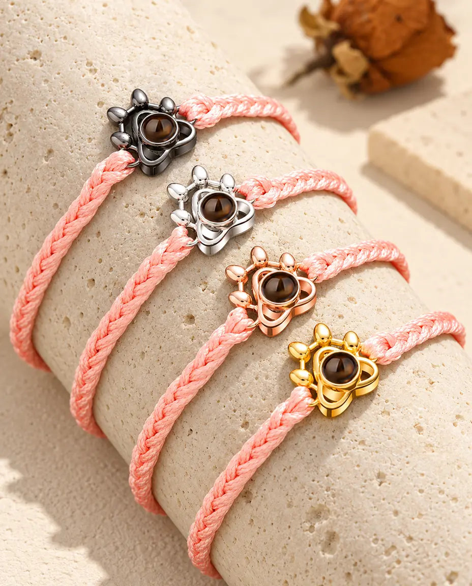 Pink braided cord paw charm bracelets showing every charm colour draped over travertine