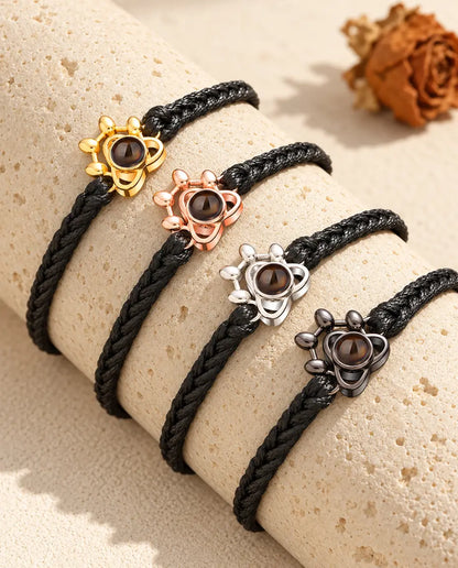 Four black braided cord bracelets with paw charms in each colour on a travertine block