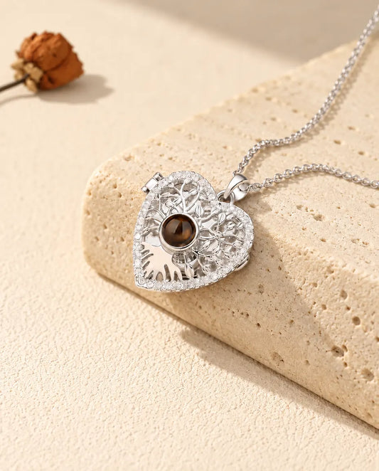 Personalised tree of life heart locket necklace in silver tone with a brown projection stone, resting on a travertine block