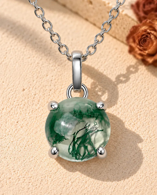 Round Moss Agate Solitaire Necklace in 925 Sterling Silver - lying on a cream textured surface beside a travertine block